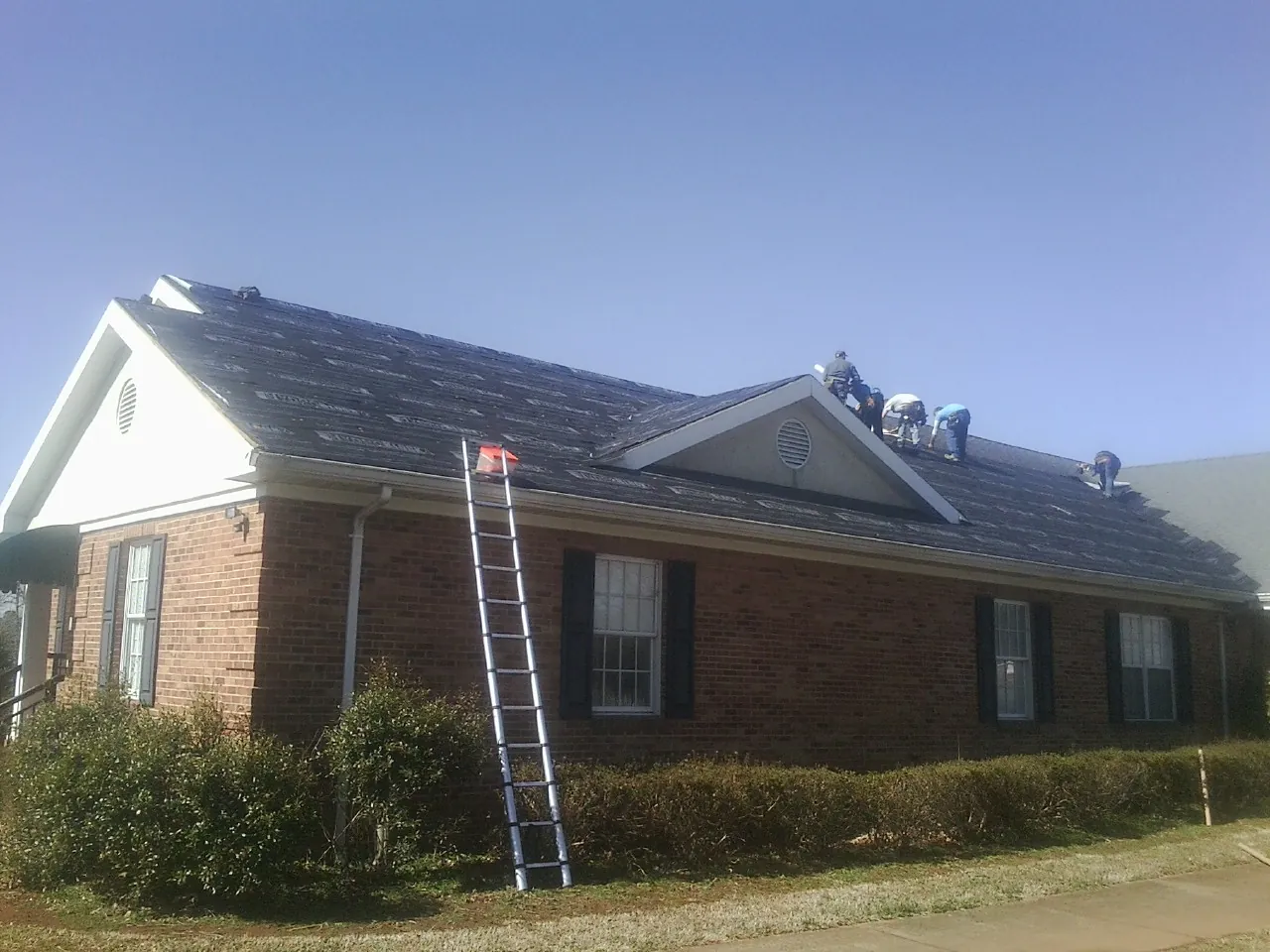 Crew tearing shingles off a brick ranch roof with a ladder set — Emergency Roof Repair work by our crew in West Cornwall