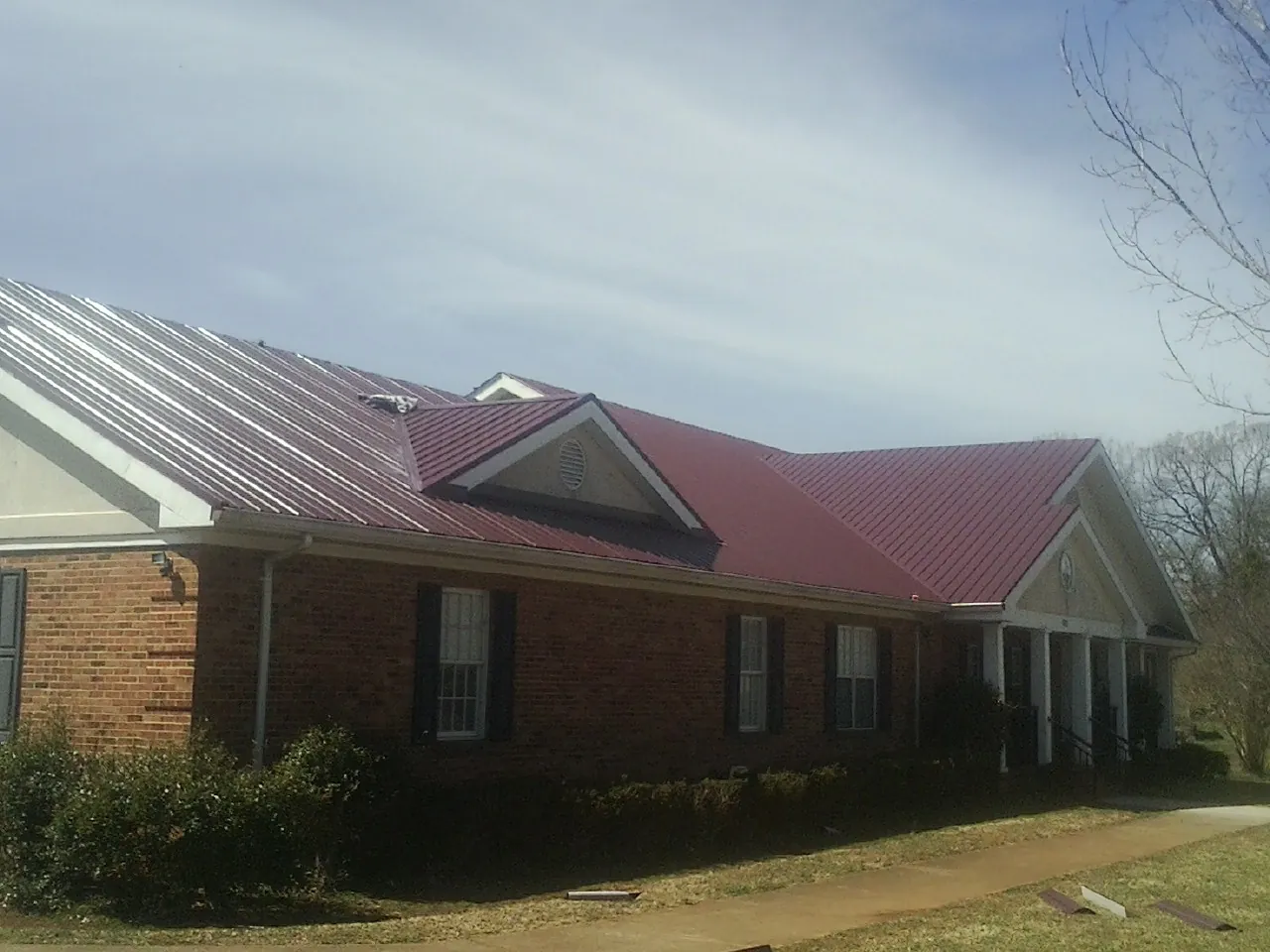 Red metal roof with gabled entries on a long brick building, from a Hail Damage Roof Repair job in West Cornwall