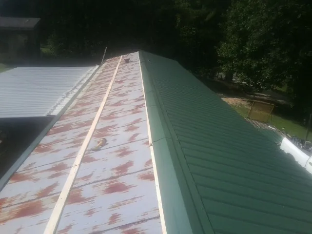 Old rusted panels beside newly installed green metal roofing — Wind Damage Roof Repair by Roofing Brothers in West Cornwall