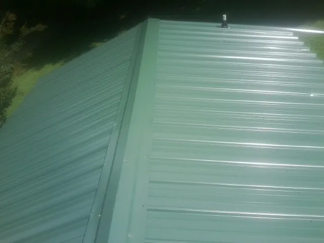 New green metal panels meeting at the ridge of a roof — Flat Roof Repair work by our crew in West Cornwall