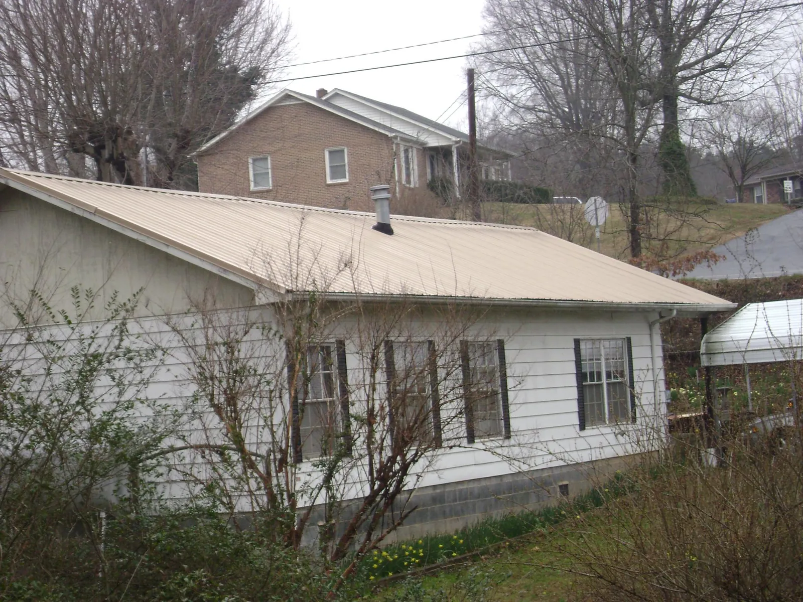 Tan metal roof on a white sided house set into a hillside — Commercial Roofing by Roofing Brothers in West Cornwall